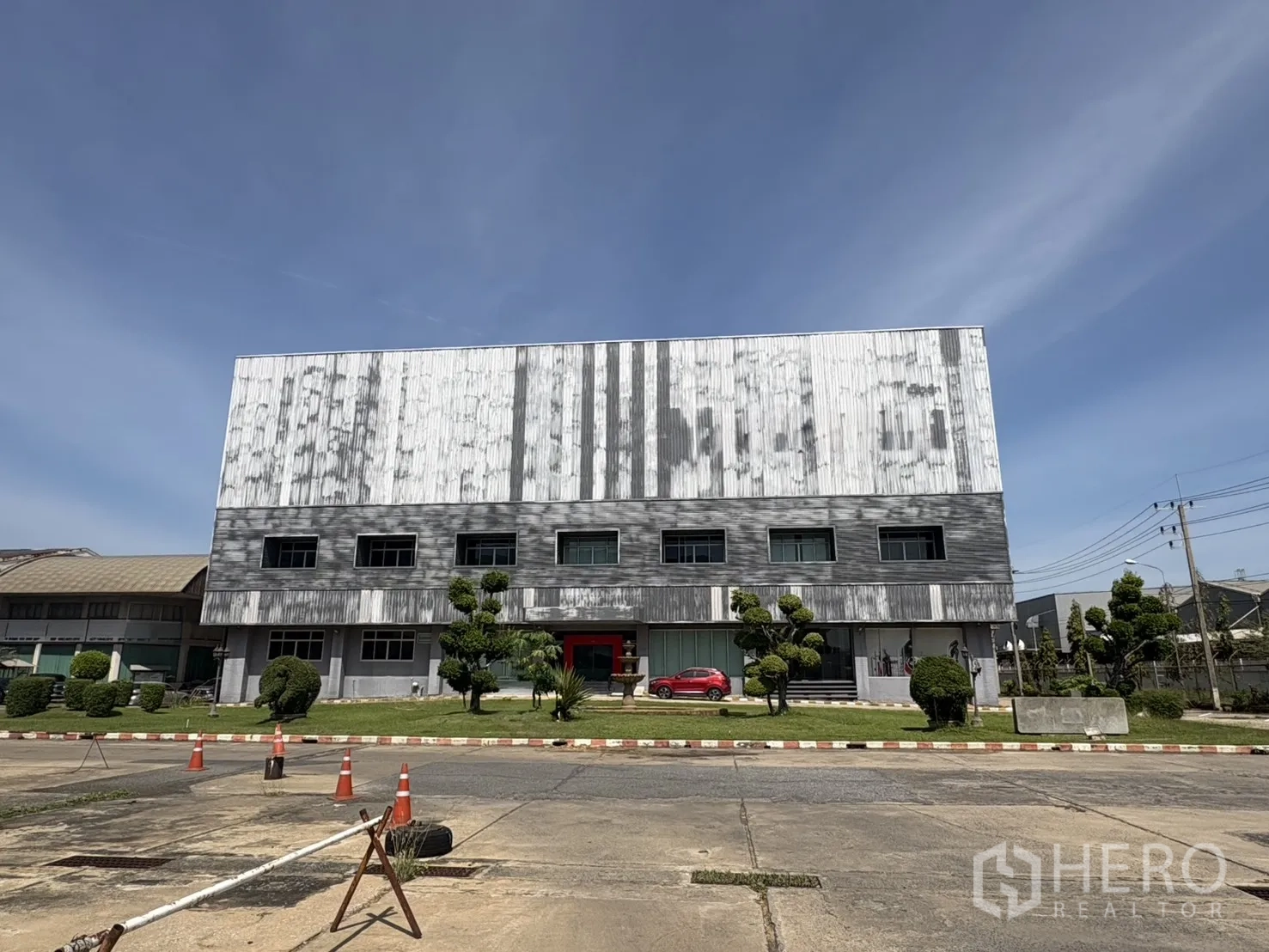 工厂 for rent in Lat Krabang, Bangkok - 三层金属外墙工业厂房，带办公窗、前方绿化草坪与宽阔混凝土广场，晴空下的曼谷Lat Krabang。