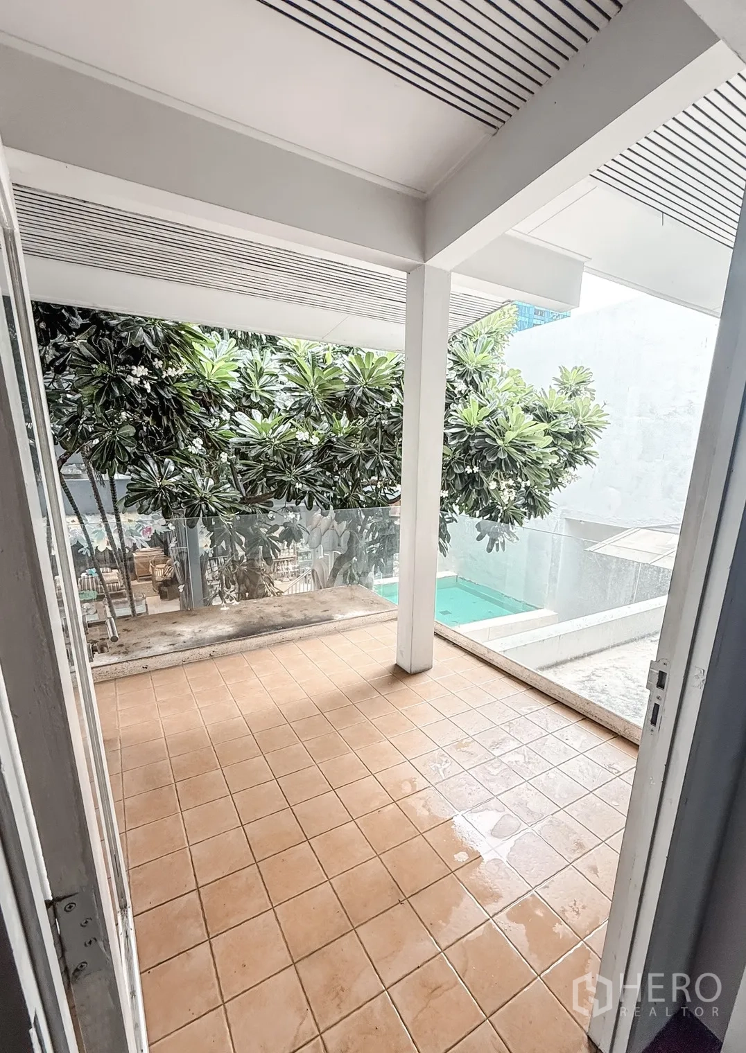家庭办公室 for rent in Watthana, Bangkok - 带顶棚的瓷砖露台，白色立柱与绿植，玻璃护栏可望见泳池。