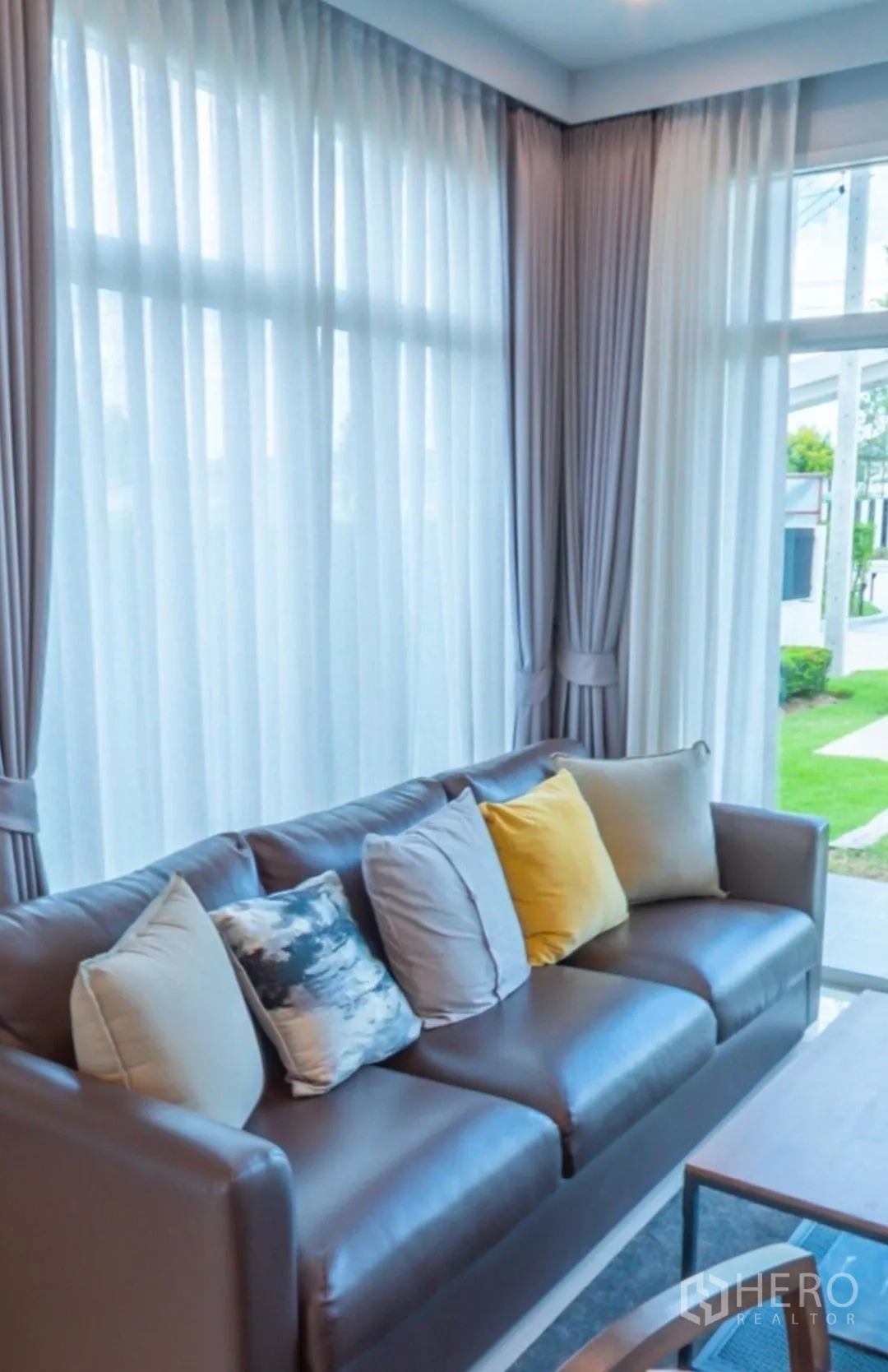 独栋房屋 for rent in Lam Luk Ka, Pathum Thani - 客厅沙发近景，旁有落地窗帘与室外草坪景色。