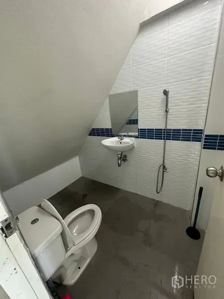 Home Office for rent in Phra Khanong, Bangkok - Compact restroom beneath the stairs with a shower spray, sink and white wall tiles.