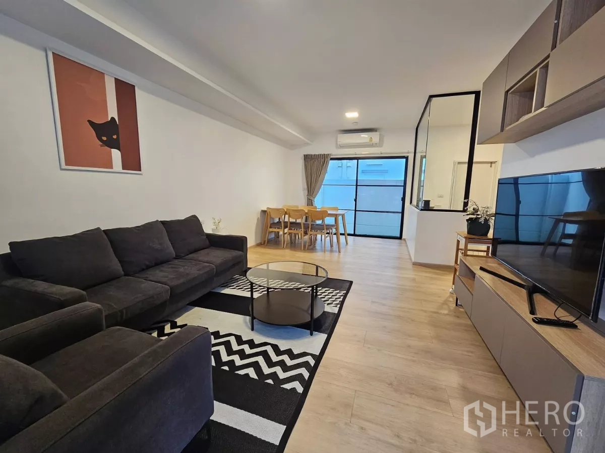 Townhouse for rent in Bang Phli, Samut Prakan - Open-plan living and dining area with dark sofa set, TV wall, and glass doors