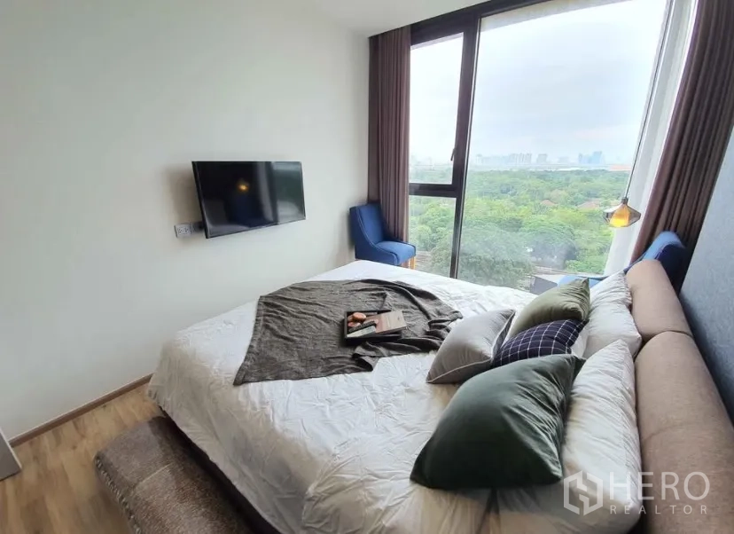 Condominium for rent in Chatuchak, Bangkok - Bedroom with large window, upholstered bed, two chairs and a wall-mounted TV.