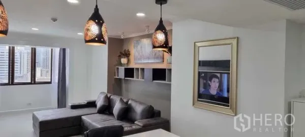 公寓 出租在Khlong Toei, Bangkok - 采光良好的客厅配L形沙发、壁挂置物架与装饰吊灯。