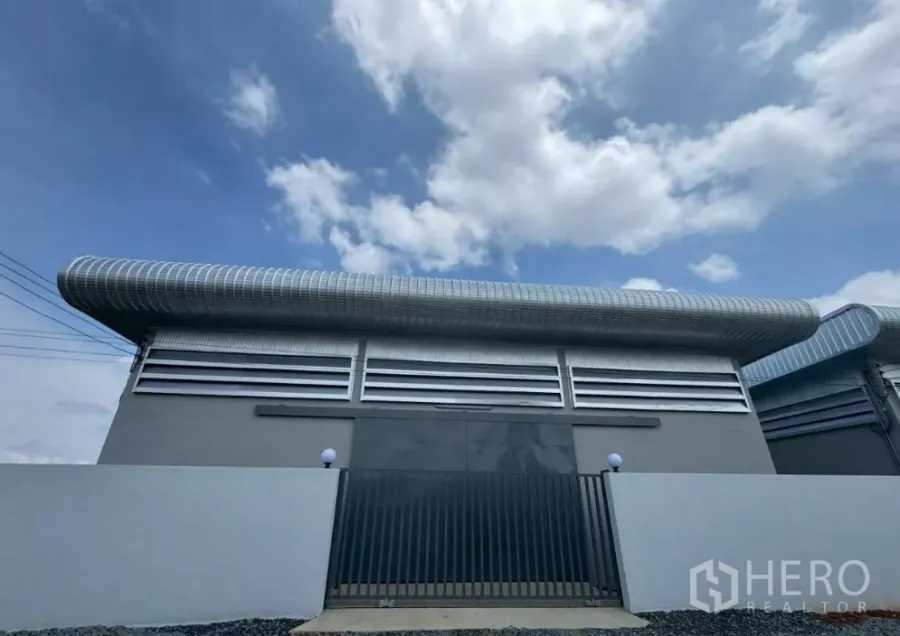 Warehouse for rent or sale in Nong Chok, Bangkok - Modern warehouse exterior in Nong Chok, Bangkok with gated entrance, louvered ventilation and a curved insulated roof under blue sky.