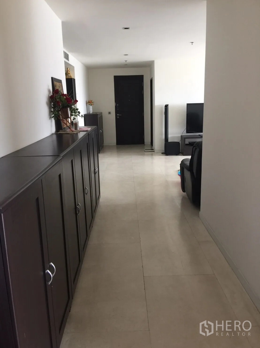 Condominium for rent in Watthana, Bangkok - Long corridor with dark wood cabinets and light tile flooring leading to the entrance.