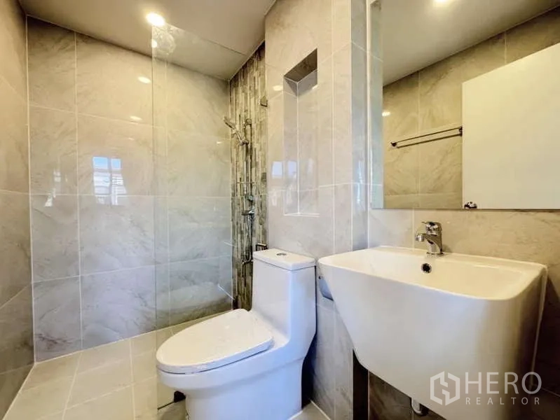 Townhouse for rent in Min Buri, Bangkok - Third bathroom finished in beige marble-style tiles with shower niche, toilet and basin.