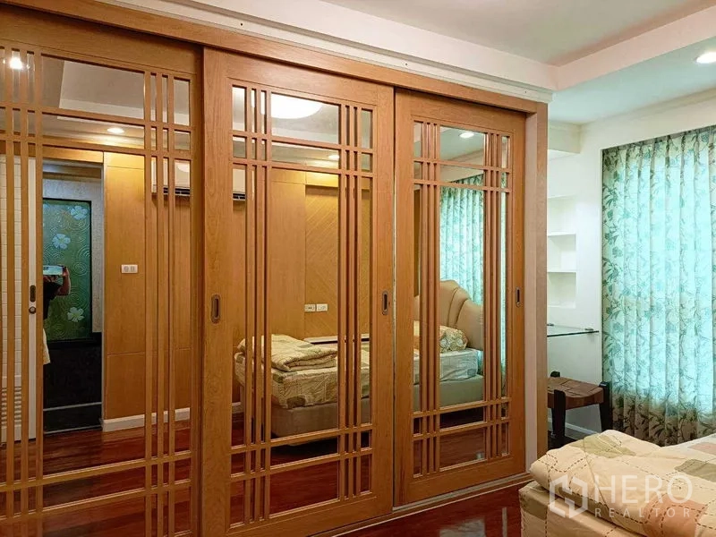 คอนโด ให้เช่าในWatthana, Bangkok - ผนังตู้เสื้อผ้าห้องนอนบานเลื่อนไม้กระจกเงา สะท้อนเตียงและโทนไม้อบอุ่น.