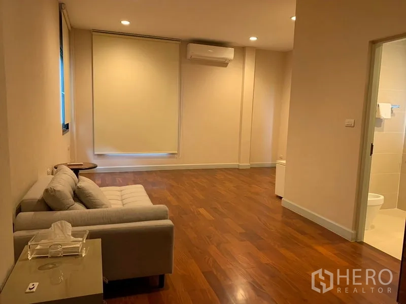 Detached House for rent or sale in Khan Na Yao, Bangkok - Spacious bedroom lounge with wood floors, sofa, air conditioner and ensuite door.