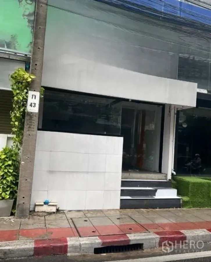 零售空间 出租在Watthana, Bangkok - 紧凑型店面，现代白色外立面，抬高入口台阶，整面展示玻璃朝向街道。