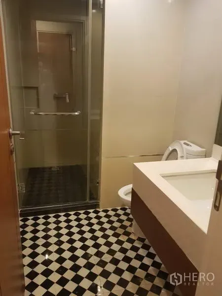 Condominium for rent in Watthana, Bangkok - Bathroom with checkered tile floor, glass-enclosed shower, wide vanity, and toilet.