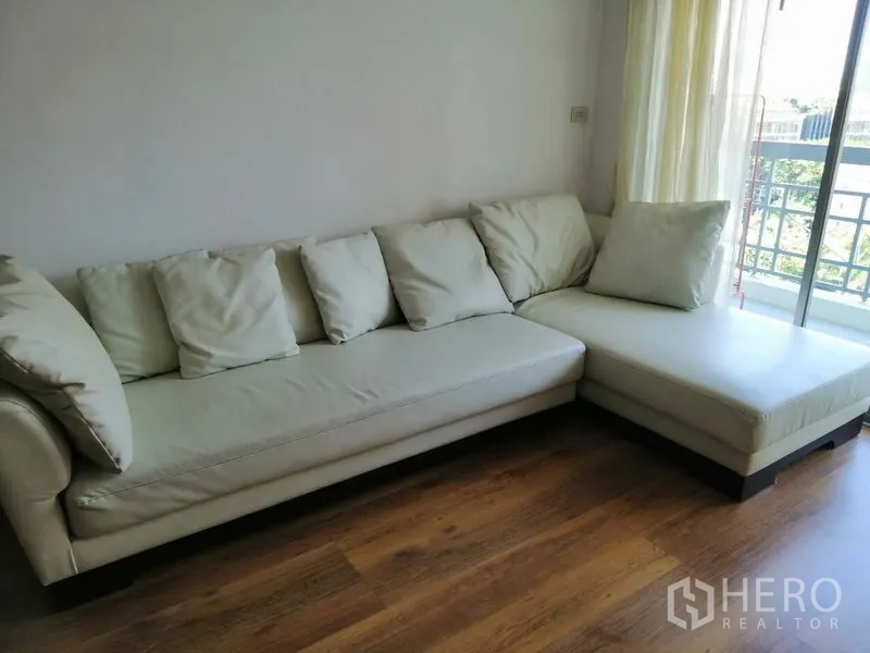 Condominium for rent in Watthana, Bangkok - Bright living room with cream L-shaped sofa beside balcony doors.