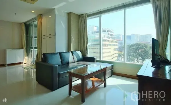 Condominium for sale in Watthana, Bangkok - Bright living room with large windows, city view, black sectional sofa and glass coffee table.