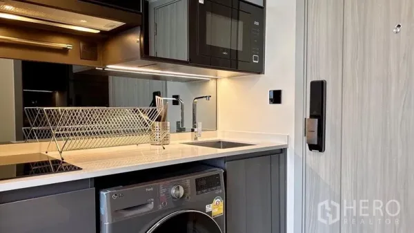 Condominium for rent - Compact modern kitchenette with stone countertop, induction hob, built-in microwave and a washer–dryer under the counter.