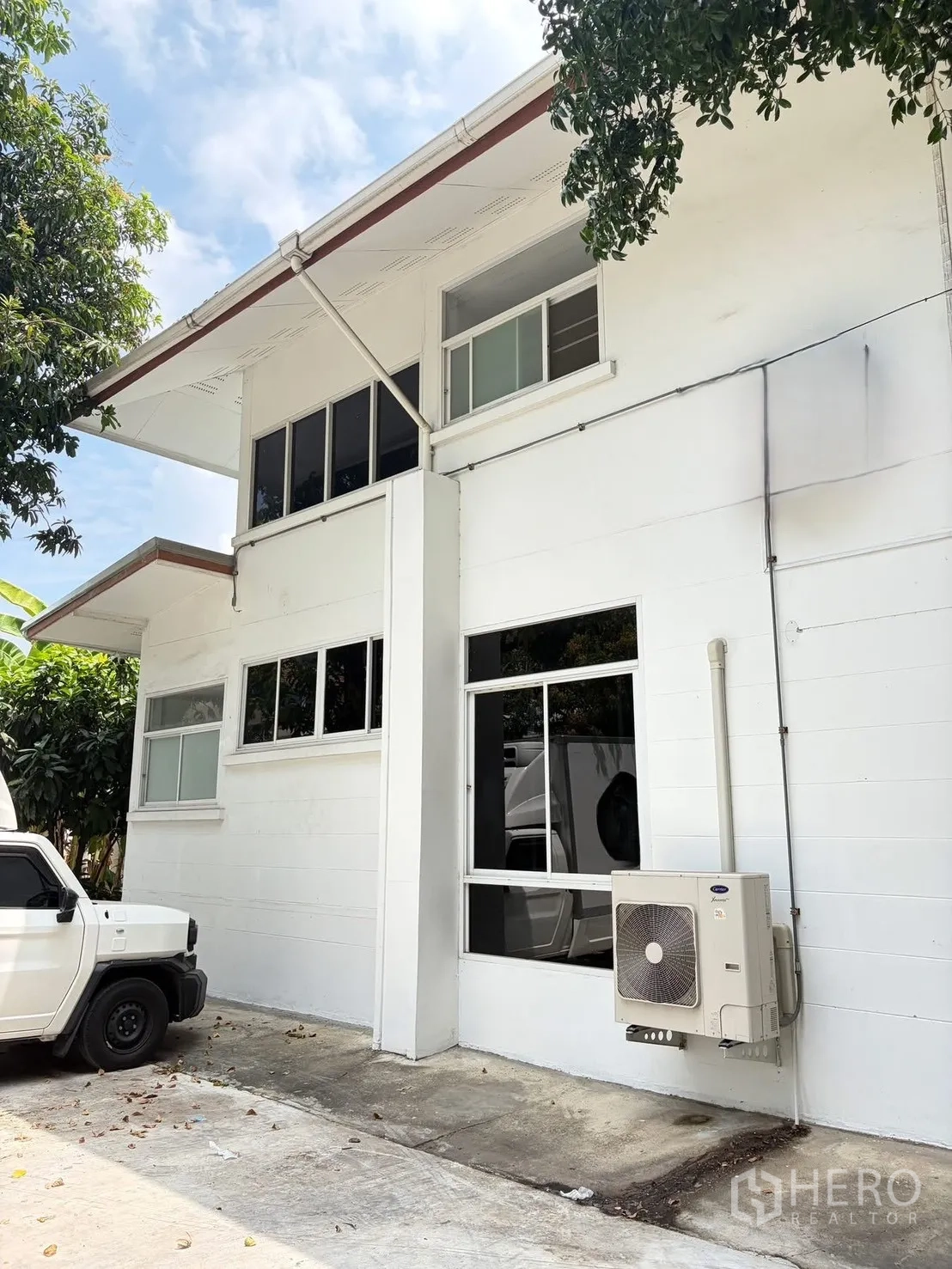 Detached House for rent in Watthana, Bangkok - Close-up of the facade with large windows and a wall-mounted AC unit beside the parking area.