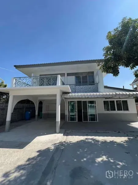 บ้าน ให้เช่าในBang Na, Bangkok - ภาพหน้าบ้านสองชั้นพร้อมที่จอดรถในร่ม ราวระเบียงลาย และลานคอนกว้างใต้ท้องฟ้าใส