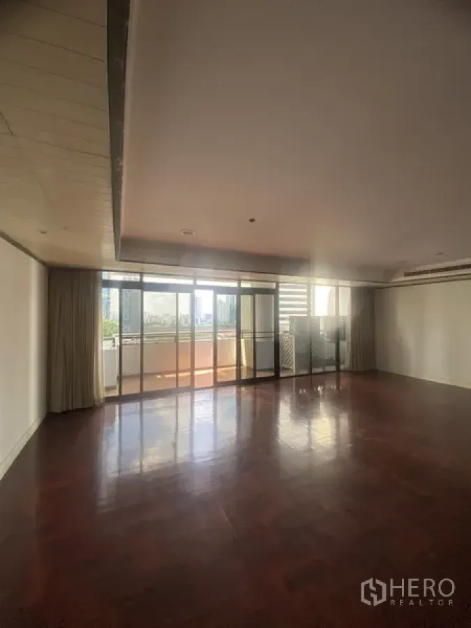Condominium for rent or sale in Watthana, Bangkok - Spacious living room with dark wood floors and floor-to-ceiling glass doors opening to a balcony with city view.