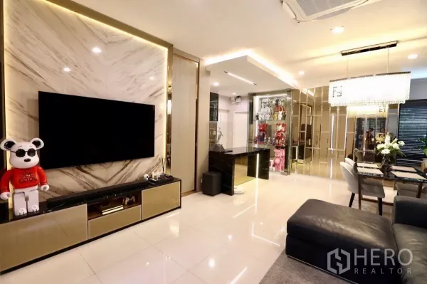 Detached House for rent in Samut Prakan - Luxurious living room featuring a marble TV wall, large screen, glossy floors and designer lighting.