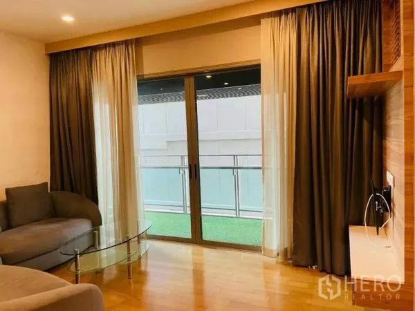 Condominium for rent in Watthana, Bangkok - Cozy living room with sofa, glass coffee table, and sliding doors to a balcony with turf.