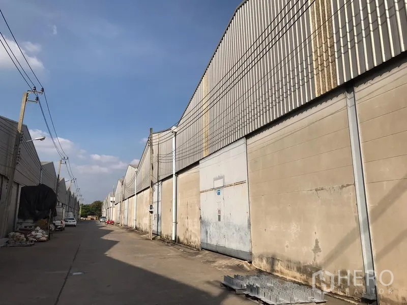 货栈 出租在Bang Phli, Samut Prakan - 仓库侧立面，金属卷门沿宽阔通道分布，架空电线清晰可见。