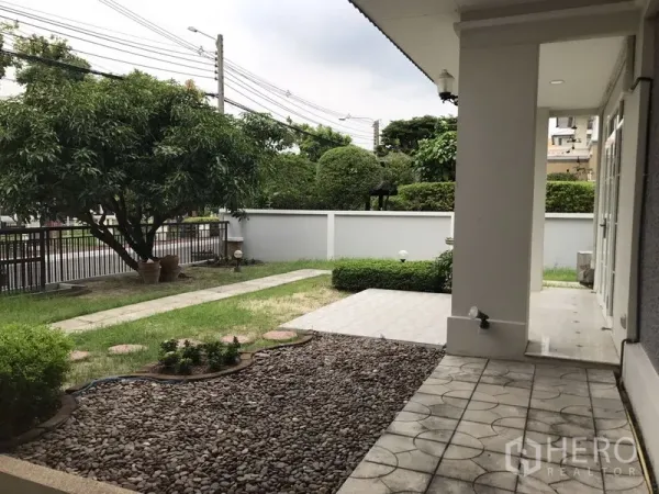 独立式住宅 出租在Phra Khanong, Bangkok - 前院花园有草坪、乔木、石径和侧边遮蔽露台。