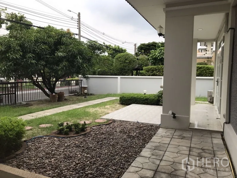 独立式住宅 出租在Phra Khanong, Bangkok - 前院花园有草坪、乔木、石径和侧边遮蔽露台。