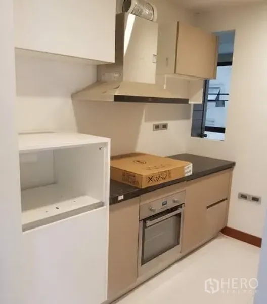Apartment for rent in Khlong Toei, Bangkok - Compact modern kitchen with built-in oven, range hood, and upper cabinets in a bright apartment.
