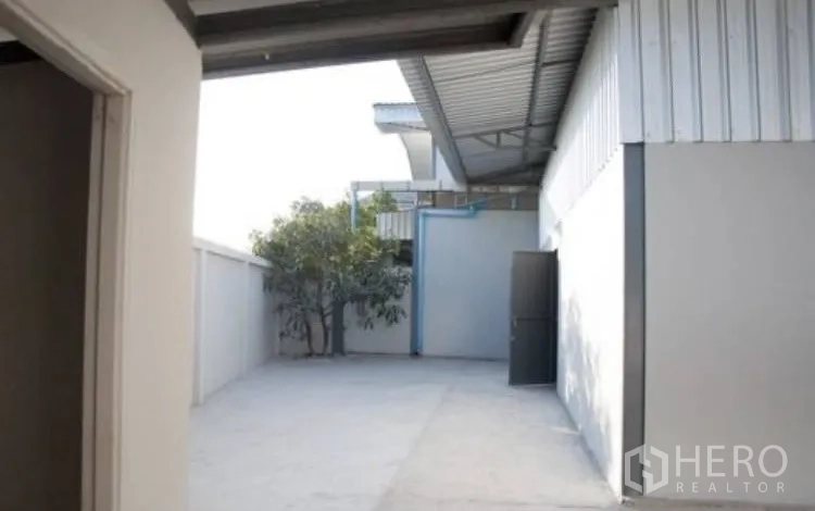 Warehouse for rent in Bang Phli, Samut Prakan - Side yard under roof overhang with access door and boundary wall.
