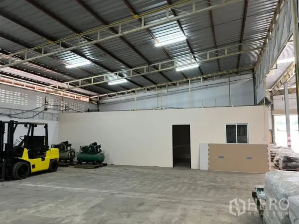 Warehouse for rent in Suan Luang, Bangkok - Warehouse floor with forklifts, air compressors and an internal office beneath a skylit steel structure.