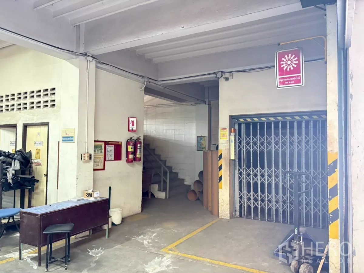 工厂 出租或出售在Bang Khun Thian, Bangkok - 底层设折叠门货梯、楼梯与安全标识的区域。