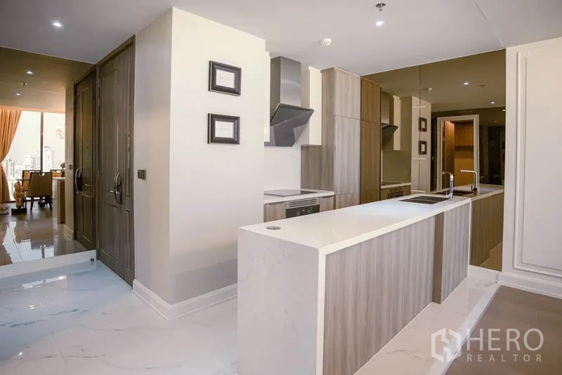 Condominium for rent or sale in Watthana, Bangkok - Kitchen perspective toward entry with island counter, marble floors and living area beyond.