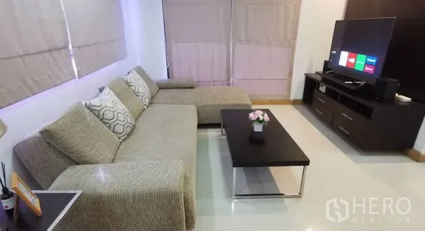 Condominium for rent in Watthana, Bangkok - Cozy living area with L-shaped sofa, coffee table, and TV console.