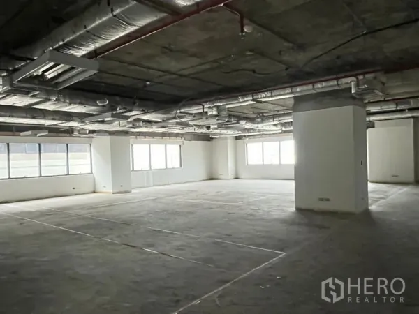 Office Space for rent - Open-plan office space with concrete flooring grid, corner windows, and exposed HVAC and sprinkler pipes.