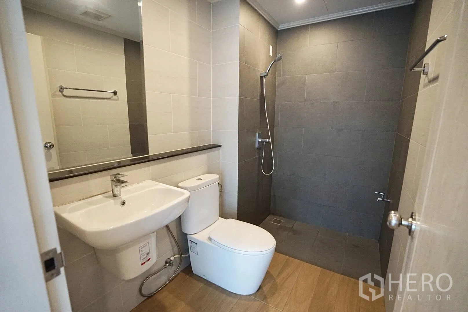 Townhouse for rent in Bang Kapi, Bangkok - Contemporary bathroom with walk-in shower, large mirror, white basin and toilet in grey tiles.