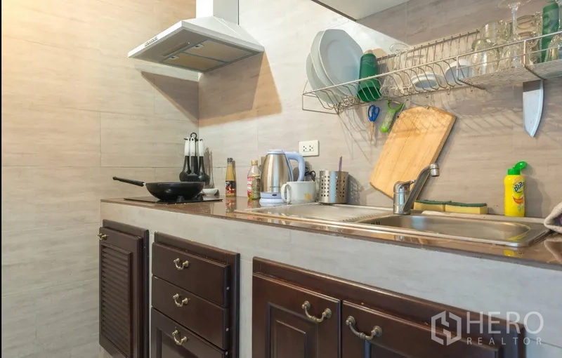 Condominium for rent in Pathum Wan, Bangkok - Kitchen countertop with double sink, range hood and dark wood cabinets.