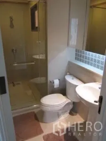 Condominium for rent in Khlong Toei, Bangkok - Modern bathroom with glass-enclosed shower, vanity sink and toilet.