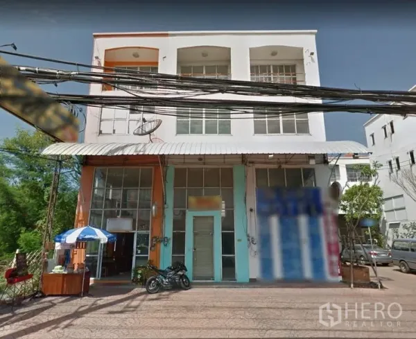Shophouse for sale in Lam Luk Ka, Pathum Thani - Facade of a multi-storey shophouse block with wide glass frontage, roller shutter and awning.