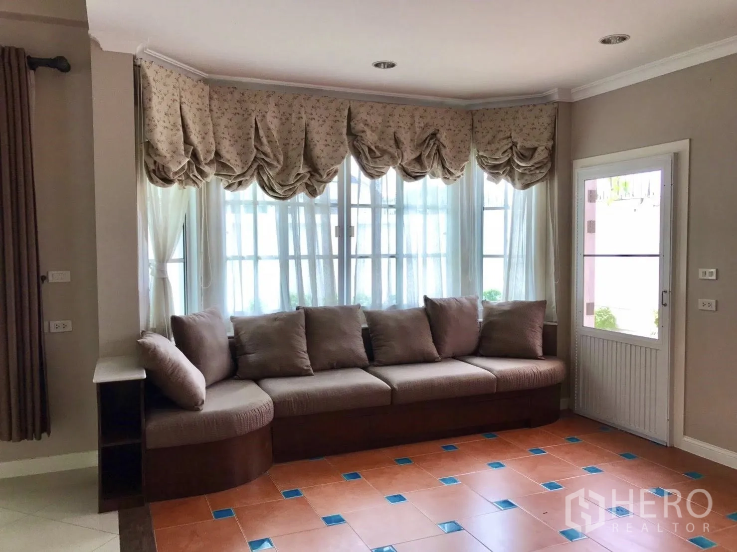 Detached House for rent in Mueang Samut Prakan, Samut Prakan - Sitting area with brown sectional sofa, draped valances and a door to the garden.