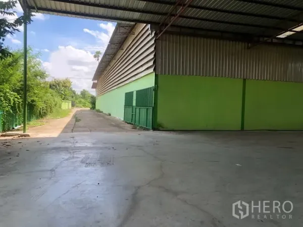 Factory for rent in Sam Khok, Pathum Thani - Open loading area with green sliding gate and side driveway next to the warehouse.