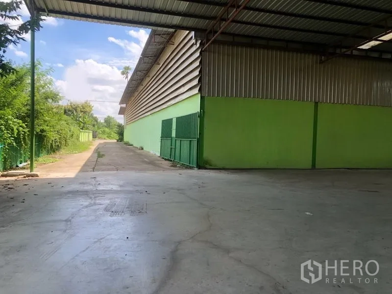 Factory for rent in Sam Khok, Pathum Thani - Open loading area with green sliding gate and side driveway next to the warehouse.
