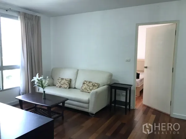 Condominium for rent in Watthana, Bangkok - Cozy living room with a cream sofa and coffee table beside a window, opening to the bedroom.