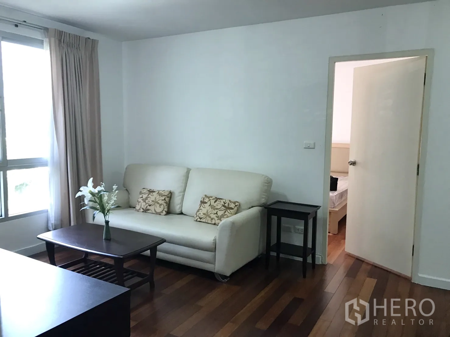 Condominium for rent in Watthana, Bangkok - Cozy living room with a cream sofa and coffee table beside a window, opening to the bedroom.