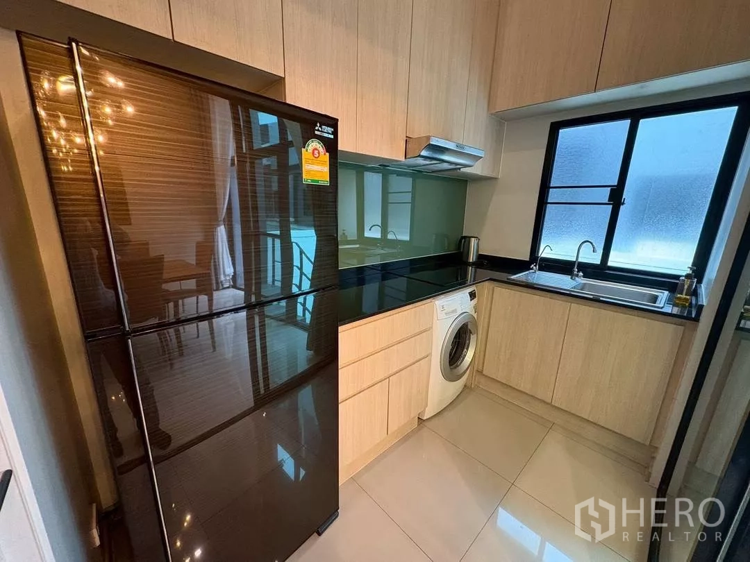 ทาวน์เฮาส์ ให้เช่าในSuan Luang, Bangkok - ครัวบิวท์อินกะทัดรัด ตู้ไม้โทนอ่อน เคาน์เตอร์สีดำ ตู้เย็นสีดำ และเครื่องซักผ้า.