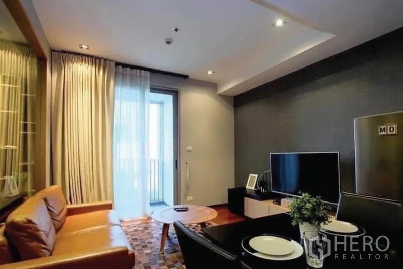 คอนโด ขายในKhlong Toei, Bangkok - ห้องนั่งเล่นอบอุ่น โซฟาหนังสีน้ำตาล ทีวี และประตูกระจกออกระเบียง