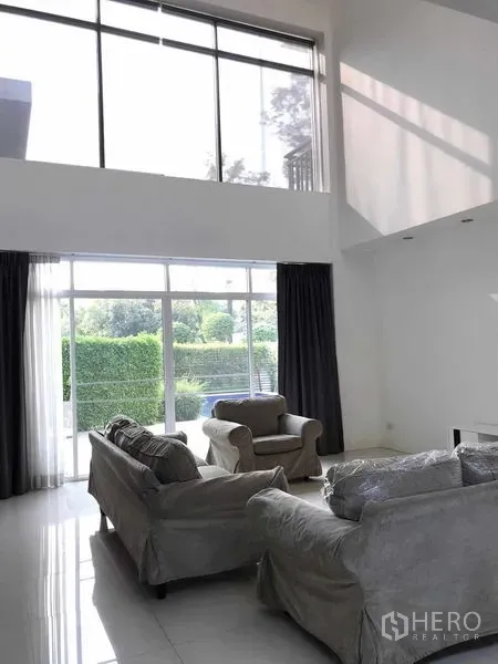 บ้าน ขายในWang Thonglang, Bangkok - ห้องนั่งเล่นเพดานสูง ผนังกระจกเต็มบาน มองสวน พร้อมโซฟาสีเทา