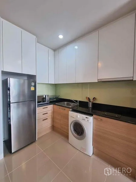 公寓 出租在Ratchathewi, Bangkok - L形现代厨房，白色橱柜、黑色台面，冰箱与洗衣机。