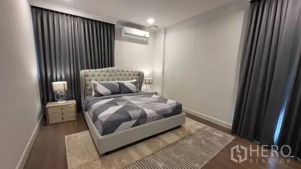 Detached House for rent or sale in Saphan Sung, Bangkok - Guest bedroom with tufted headboard, gray curtains, bedside lamps and wood flooring.