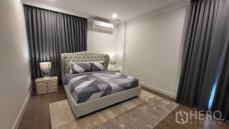 Detached House for rent or sale in Saphan Sung, Bangkok - Guest bedroom with tufted headboard, gray curtains, bedside lamps and wood flooring.