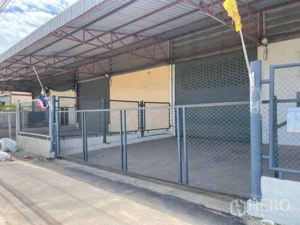 工厂 出租在Lat Lum Kaeo, Pathum Thani - 带金属屋顶的抬高装卸月台，两个卷闸门与封闭前院的斜向视图。