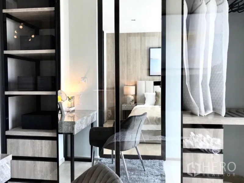 Condominium for rent or sale in Pathum Wan, Bangkok - Walk-in closet with open shelving and mirrored doors, marble desk and grey chair facing the bedroom.