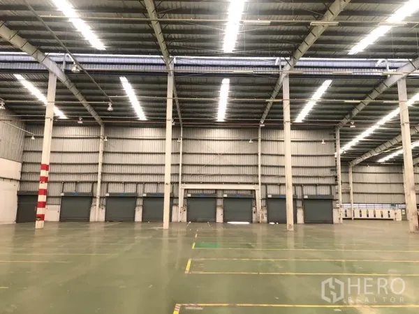工厂 出租在Phra Nakhon Si Ayutthaya - 厂房内部朝向装卸门的视角，条形照明明亮均匀。